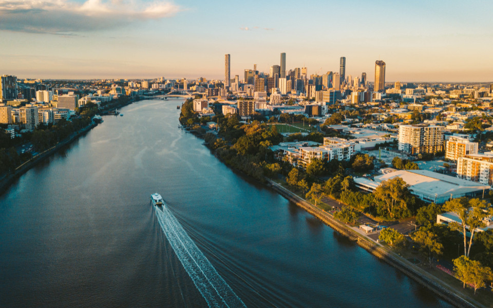 Luftaufnahme von Brisbane bei Sonnenuntergang, während ein Boot am Brisbane River auf die Stadt zusteuert