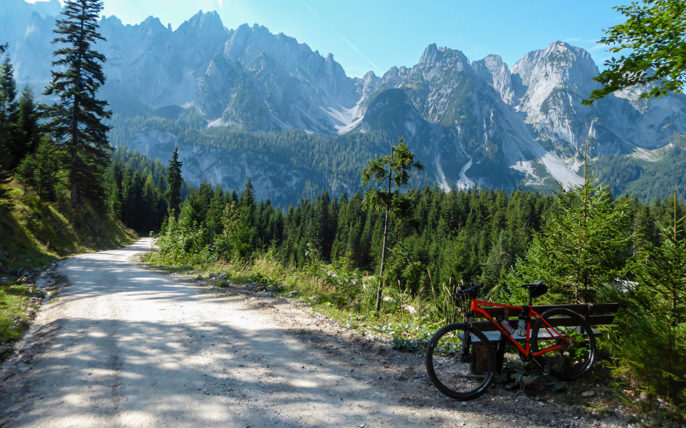 Oranges Fahrrad lehnt an einer Parkbank im Salzkammergut mit Blick auf die Alpen bei Sonnenschein