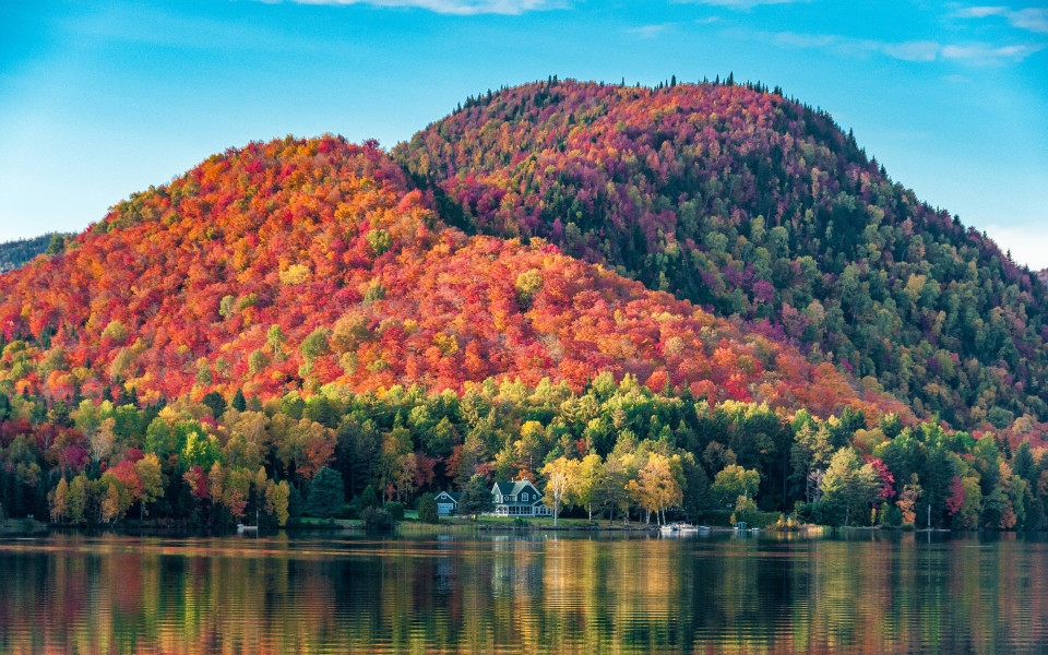 Die mit roten Ahornwäldern bedeckten Hügel hinter einem Holzhaus am Ufer eines Sees in Quebec, an einem wunderschönen Herbstabend.