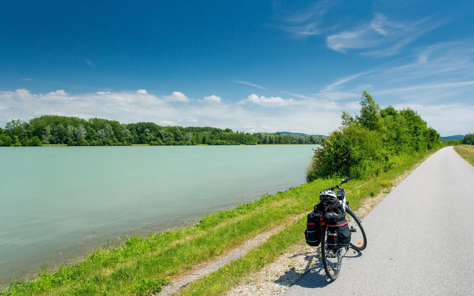 Fahrrad mit Gepäck auf dem Donauradweg mit Blick auf die Donau und umliegende grüne Landschaft